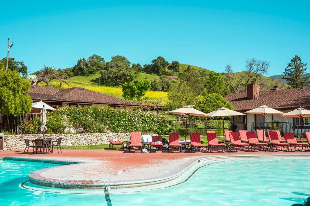A pool with red chairs and rolling green hills in the background.